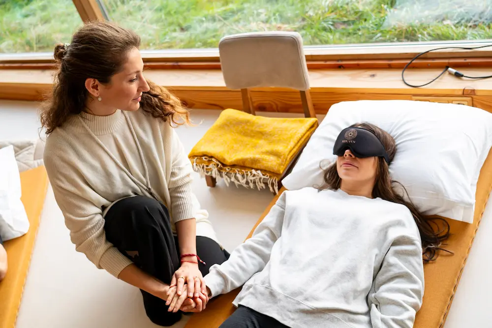 A facilitator holding the hand of a participant resting with an eye mask during a session