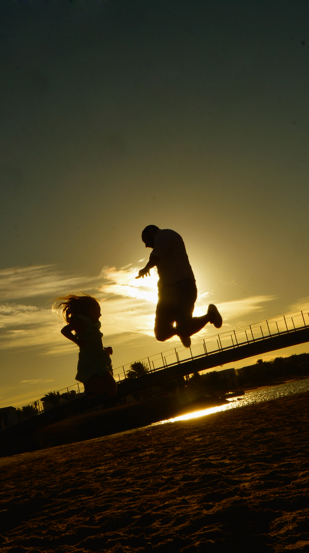 Two silhouettes leaping joyfully at sunset